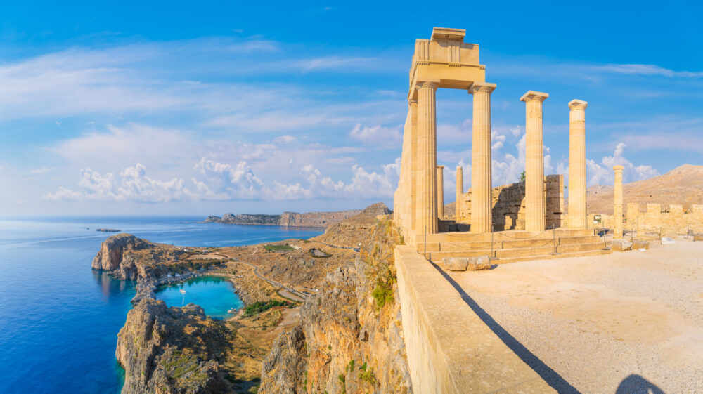 Ancient Greek temple ruins overlooking a coastal landscape with blue sea and rugged cliffs.