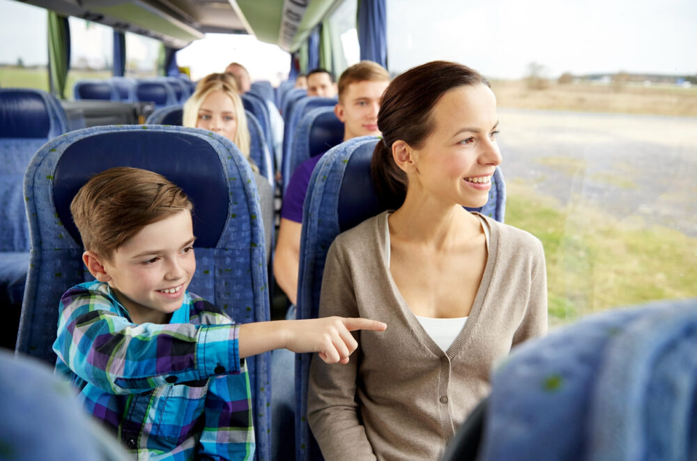 A woman and a boy sit on a bus, smiling and pointing out the window.