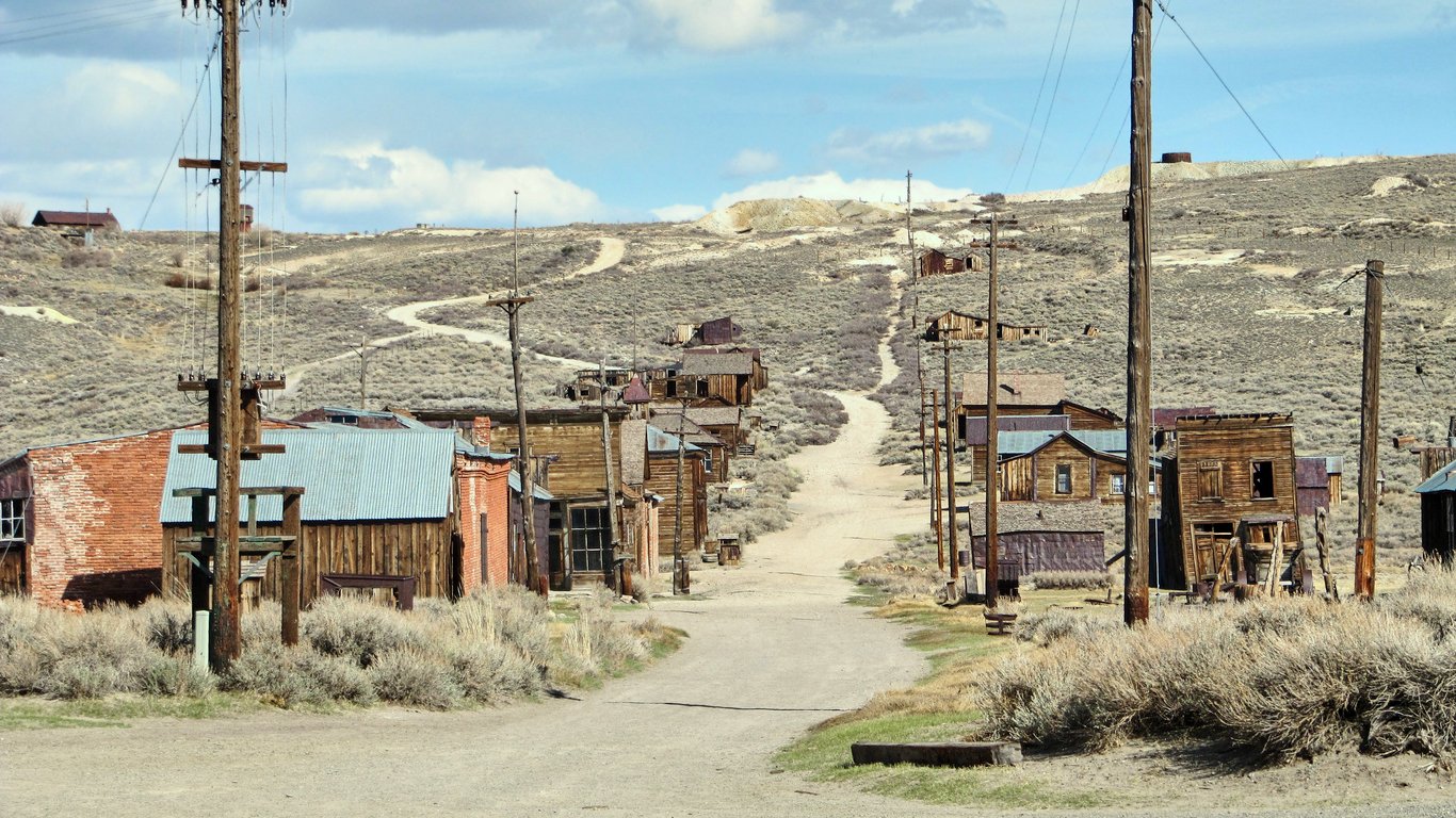 Dirt road leading through an abandoned ghost town with weathered wooden buildings and telephone poles.