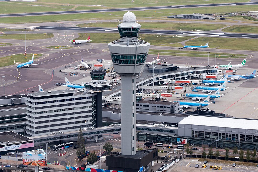 Aerial view of an airport control tower with surrounding airplanes and terminal buildings.