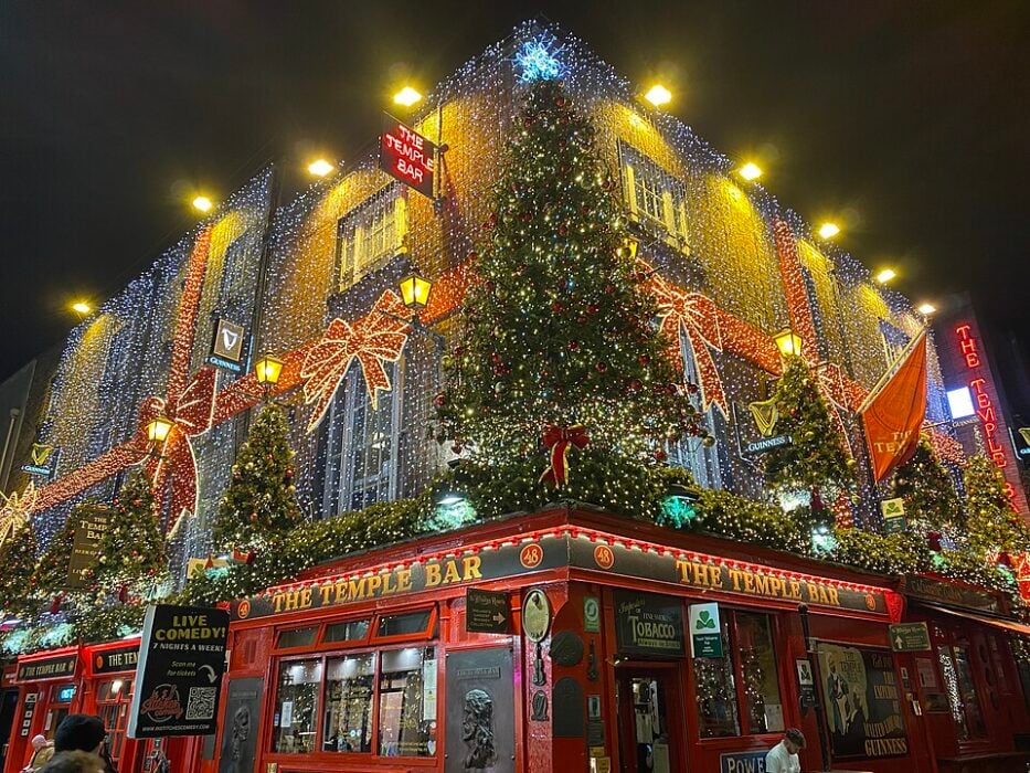 Pub exterior with festive Christmas lights, large bows, and decorated trees at night.