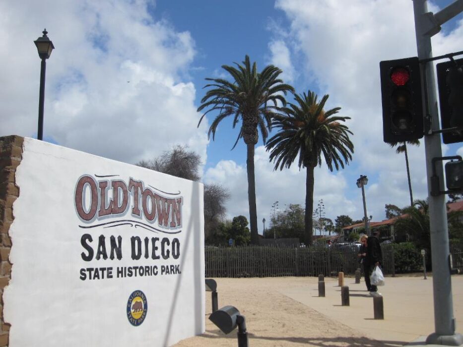 Sign reading "Old Town San Diego State Historic Park" with palm trees and cloudy sky in background.