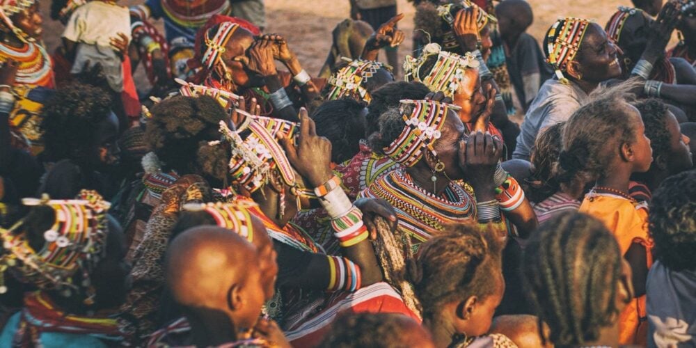 A group of people wearing colorful, beaded clothing and headdresses gathered closely together in an outdoor setting.