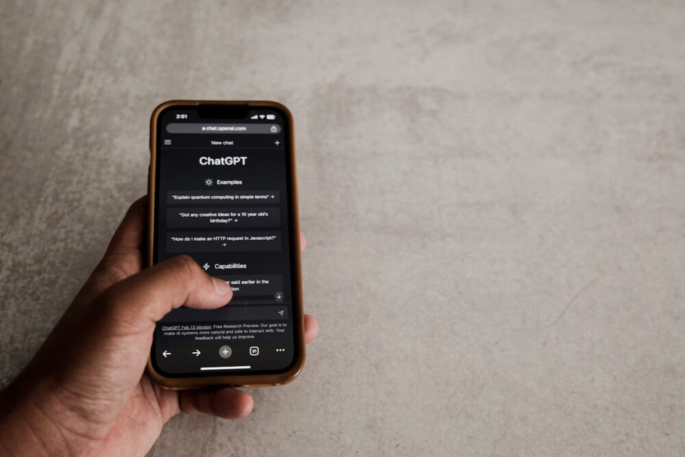 Hand holding phone displaying ChatGPT webpage with examples and capabilities listed.