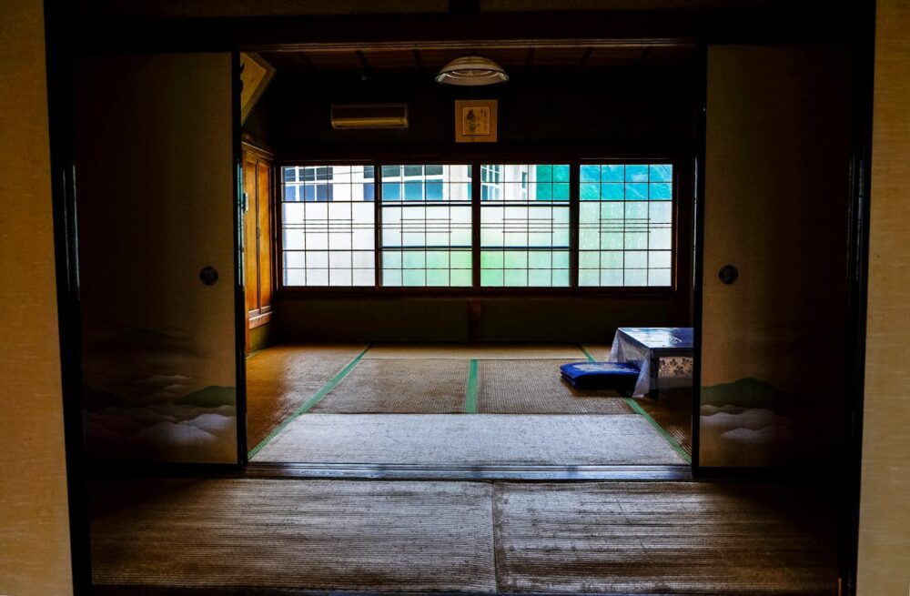 Traditional Japanese room with tatami mats, low table, cushions, and shoji screens, partially open sliding doors.