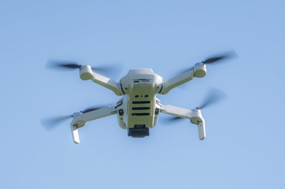 A white drone flying with spinning propellers against a clear blue sky.
