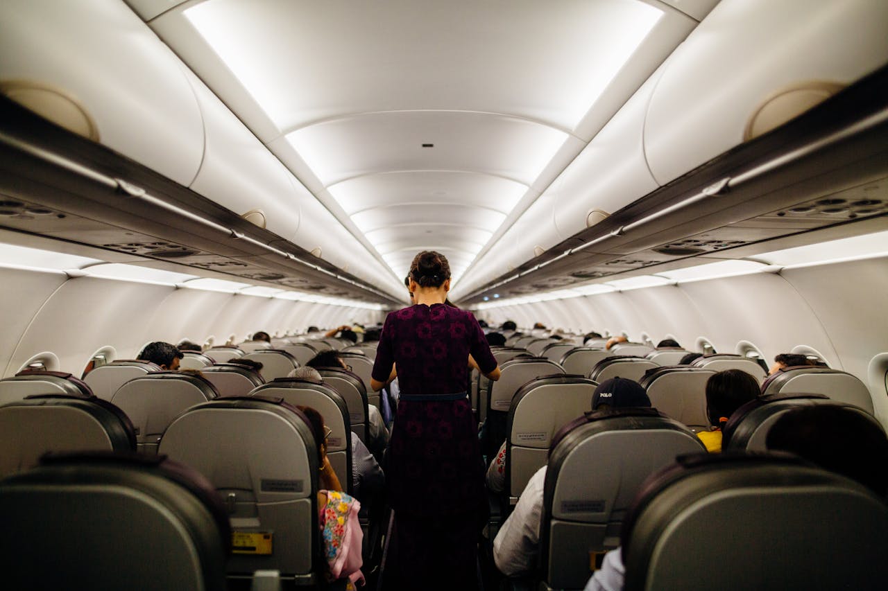Flight attendant walking down the aisle of an airplane with seated passengers.