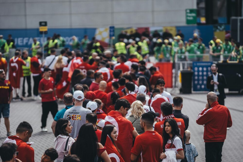 Crowd of people in red shirts lining up outside a stadium entrance with security personnel.