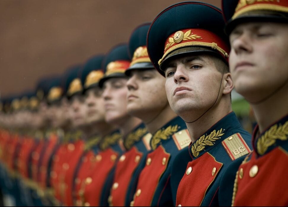 Line of soldiers in uniform with ornate hats, standing in formation, focused and serious expressions.