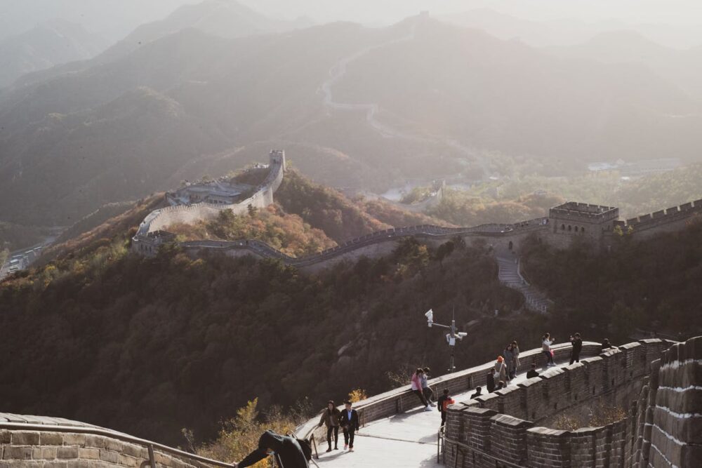 People walking on the Great Wall of China, surrounded by mountainous landscape and morning mist.