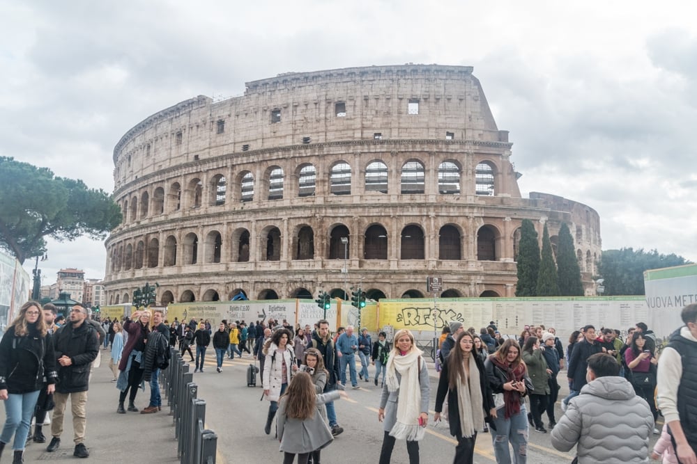 Crowd of people walking near the Colosseum in Rome on a cloudy day.