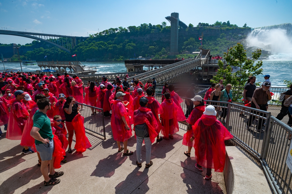 People in red ponchos walking near a dock with Niagara Falls in the background.